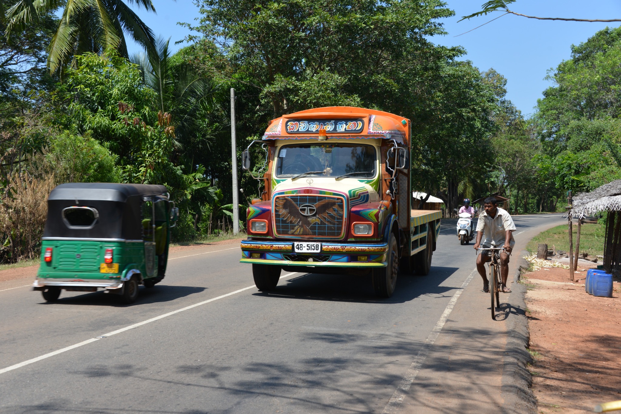 Bunter Lastwagen, Tuk-Tuk und Radfahrer auf einer Landstraße in Sri Lanka, 2016